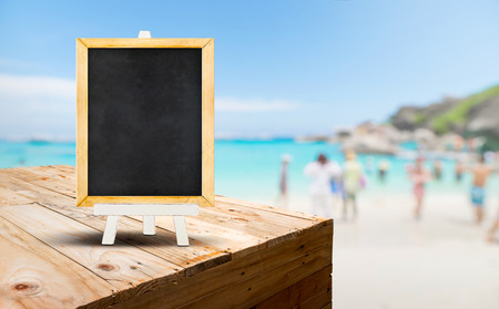 Blank blackboard on wood table food stand with blur sand beach and blue sea with traveler background.Template Mock up for summer vacation promotion saleの写真素材