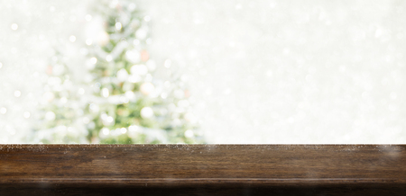 Empty dark brown wooden table top with abstract muted blur christmas tree and snow fall background with bokeh light,Holiday backdrop,Mock up banner for display or montage of productの写真素材
