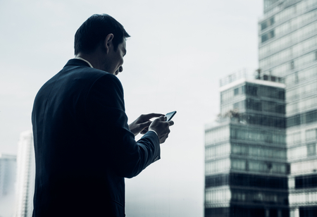businessman using mobile phone near office window at office building,online business conceptの写真素材