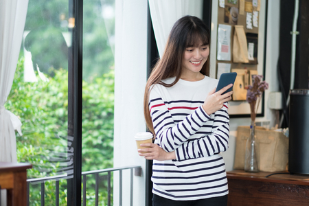 Asian woman talking on mobile phone video call and standing at cafe restaurant near window see through garden,Digital age lifestyle,Working outside office conceptの写真素材