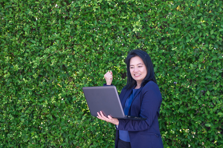 Businesswoman arm up to celebrating business plan success outside office at green leaf wallの写真素材
