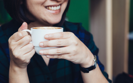 Close up woman hand holding hot cappuccino coffee cup with smiling face in cafe shop,leisure activityの写真素材
