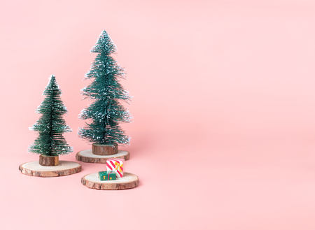 Tree Christmas tree on wood log slice with present box on pastel pink studio background.Holiday festive celebration greeting card with copy space for display of design or contentの写真素材