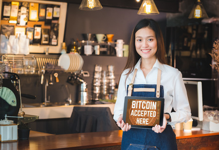 Close up woman barista holding tablet and show bitcoin accepted here on tablet screen at cafe counter bar,seller coffee shop accept payment by crypto currency.digital money concept.modern waitressの写真素材
