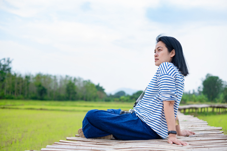 asian woman sitting cross leg on bamboo bridge at rice field at evening time feel relax and fresh with clam emotion.natural travelの写真素材