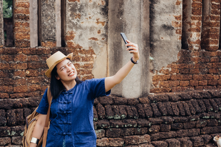 Asian tourist woman selfie at ancient of pagoda temple thai architecture at Sukhothai Historical Park,Thailand. Female traveler in casual thai cloths style visiting city conceptの写真素材