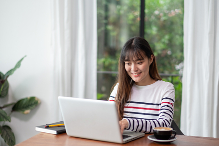 Happy asian woman using on laptop computer while working near window at cafe restaurant,Digital co working space lifestyle.influencer blogger review.working outside officeの写真素材