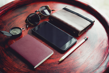 Set of mobile, passport ,notebook,sunglasses,compass and white pencil on rustic red wood round table near window.の写真素材