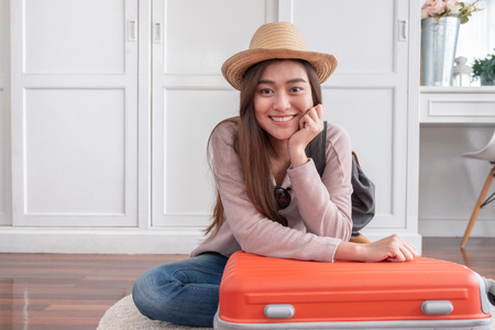Young asian woman traveler packing stuff in orange suitcase prepare for holiday vacation at home.backpacker travel conceptの写真素材