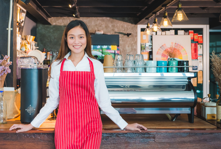 Asian female barista wear red apron at counter bar with smile face,cafe service concept,owner business start upの写真素材