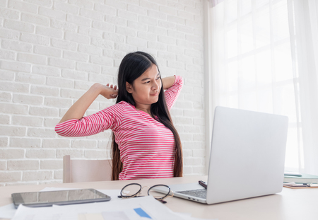 Asian woman freelancer stretching arm at back in front of laptop on desk from work in home office,work at homeの写真素材