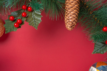 Christmas decoration and fir branches wreath with cherry and pine cone on red table background.の写真素材