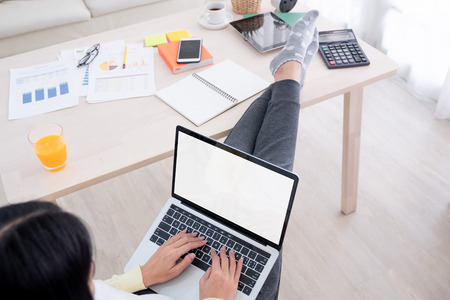 top view of woman use laptop and leg on table chill out working at home.mock up template device screen.Digital lifestyle concept.の写真素材
