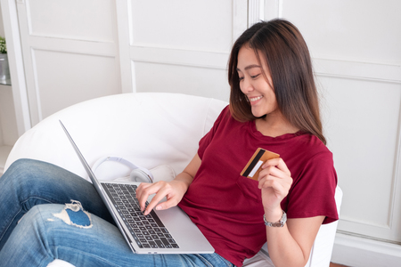 Close up woman holding credit card and use laptop shopping online on sofa in house.digital payment marketing technology conceptの写真素材