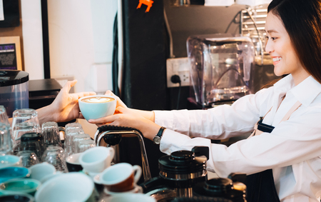 Barista served hot coffee to customer with smiling face at counter bar in cafe restaurant,coffee shop business owner concept,Service mind waitressの写真素材