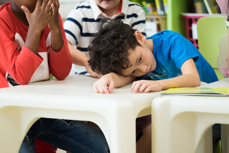Caucasion boy kid with sadness emotion sitting in classroom in kindergarten preschool.bulying depression conceptの写真素材