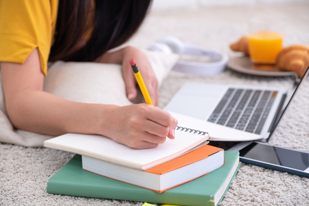 Close up woman lying on carpet and writing on notebook and learning on laptop  at home,work at home conceptの写真素材