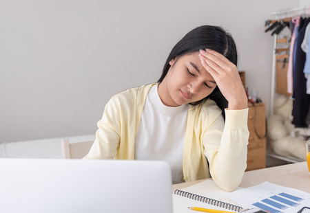 Asian female freelancer headache and stress while working with laptop on table in bedroom at home.Work at home concept.work from home conceptの写真素材