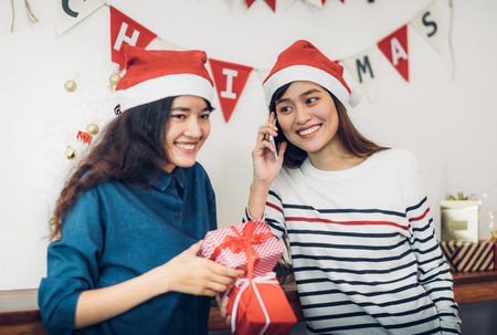 Asia girl friends wear santa hat in merry christmas party and exchange red gift box with smiling face,Xmas gift givingの写真素材