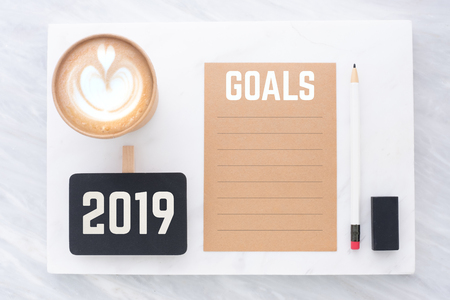 2019 goals on brown recycle paper with pencil,clip blackboard,pencil,eraser and coffee cup on white and grey marble table.mock up for adding text,new year resolution conceptの写真素材