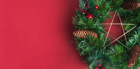 Green pine christmas wreath with star and pine cone ,cherry decoration item on red wall background.copy space for adding text or design.Celebration holiday festive greeing cardの写真素材