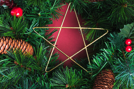 Close up star on green pine christmas wreath and pine cone ,cherry decoration item on red wall background.Celebration holiday festive greeing cardの写真素材