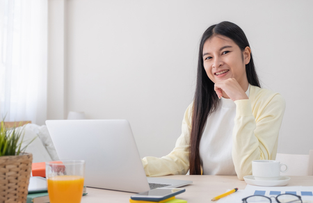 Asian female freelancer reading report on laptop on table in bedroom at home.Work at home concept.work from home.relax lifestyleの写真素材