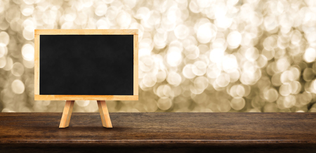 Blank blackboard on wood table with blur abstract sparkle gold background bokeh light,Mock up for display of product,Banner or header for advertise on online media,Holiday celebrateの写真素材