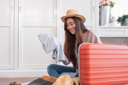 Young asian woman traveler prepare cloth into orange suitcase for holiday vacation at home.backpacker travel conceptの写真素材