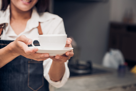 asia woman barista wear jean apron holding hot coffee cup served to customer with smiling face at bar counter,Cafe restaurant service concept.waitress workingの写真素材
