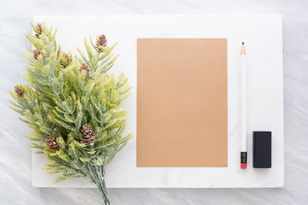 Top view of pencil, eraser,fir leaf and brown  notepad on white marble block and stack on grey marble table.Flat lay Mock up template for adding or display text or design.Stationery itemの写真素材