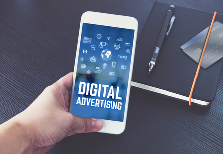 Hand holding mobile talking with digital advertising on screen with black notebook and credit card on black wooden desk,Digital marketing technology conceptの写真素材