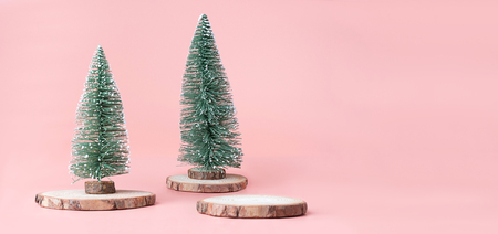 Christmas tree on wood log slice with present box on pastel pink studio background.Holiday festive celebration greeting card with copy space for display of design or contentの写真素材