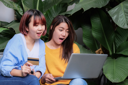 Two asia woman excited with sale promotion on website shop on laptop sitting on chair in garden at home.shopping online with credit card.Leisure digital lifestyleの写真素材