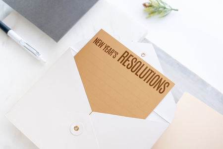 Top view of new year's resolutions on gold card in envelope with paper and pen marble table office...