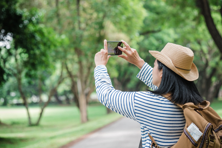 Asian woman backpack traveler use mobile take photo when traveling at rain forest.Holiday vacation concept.journey lifestyle.solo travelの写真素材