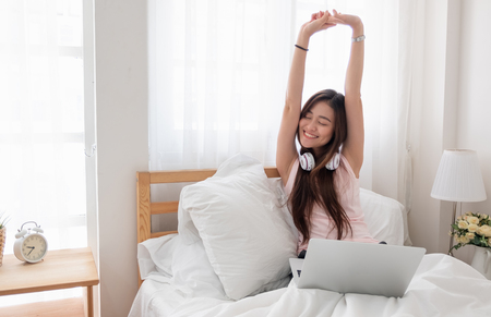Asian woman wear top tank raise arms up while using laptop on bed in bedroom in morning,relax lifestyle concept.の写真素材