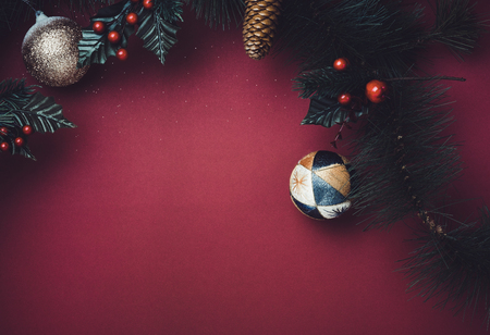 Christmas ball and fir branches for wreath with cherry and pine cone on red table background. winter holiday festive celebration conceptの写真素材