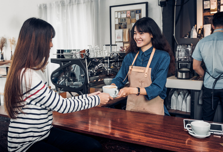 Barista served hot coffee cup to customer with smile face at counter bar in cafe restaurant,coffee shop business owner concept,Service mind waitressの写真素材