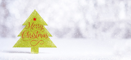 Close up Merry Christmas word on green Christmas tree with sparkling red star with snow fall on white floor at silver background bokeh light,Banner mock up for winter holiday seasonal greeting cardの写真素材