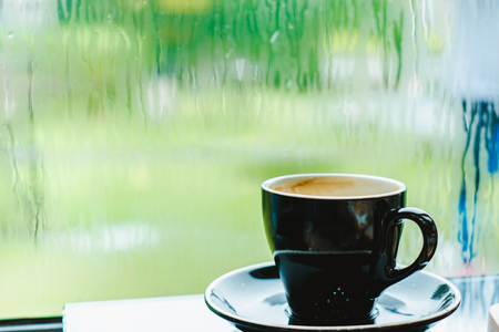 Black coffee cup on table in cafe restaurant near window in garden when raining in garden outside shop,Food and drink concept,Leisure lifestyleの写真素材
