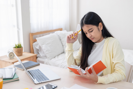 Asian female freelancer headache and stress while working on paperwork with laptop on table in bedroom at home.Work at home concept.work from home conceptの写真素材