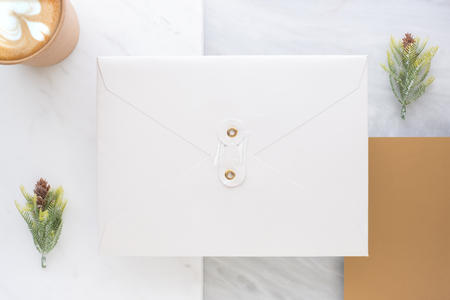 Top view of blank white envelop overlap on gold card with hot coffee cup and pine leaf on two layer step of marble table top.Mock up template for display of design .luxury business itemsの写真素材