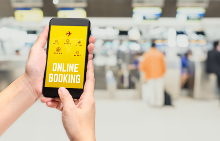 Close up hand holding mobile phone and touch on screen with online booking word with feature icon at check in airport counter blur background,Digital lifestyle Technology conceptの写真素材