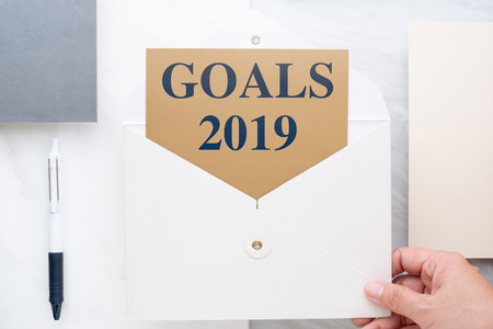 Top view of hand holding white envelop with goals 2019 new year's resolutions on gold card in envelope with paper and pen marble table office desk.Future of business planの写真素材