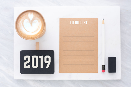 2019 to do list on brown recycle paper with pencil,clip blackboard,pencil,eraser and coffee cup on white and grey marble table.mock up for adding text,new year resolution conceptの写真素材