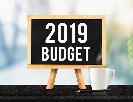 2019 budget on blackboard with easel on black marble table with coffee cup and pencil on blurred office building hall way background,New year business plan conceptの写真素材