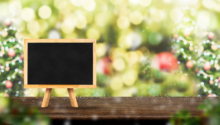 blackboard on dark brown wood table top with abstract blur christmas tree red decor ball and snow fall background with bokeh light,winter Holiday banner,Mock up for display of productの写真素材