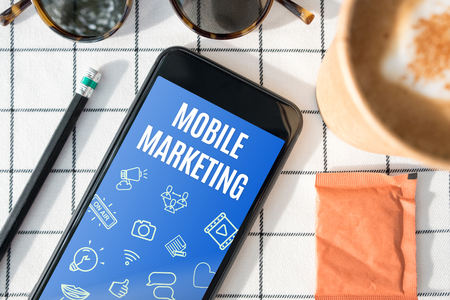 top view mobile marketing feature on mobile screen with coffee cup,sunglasses,pencil on white table cloth.digital advertisingの写真素材