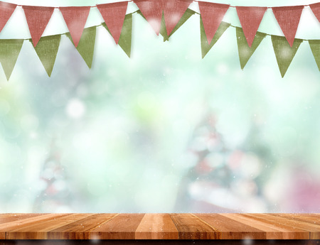 Empty wooden table and red green banner flag with abstract blur christmas tree and snow falling background with bokeh,Holiday backdrop,Mock up banner for display of product for promotion onlineの写真素材